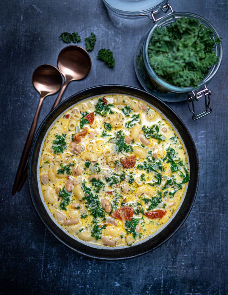 Photo of pasta e fagioli soup in bowl with kale and gold spoons