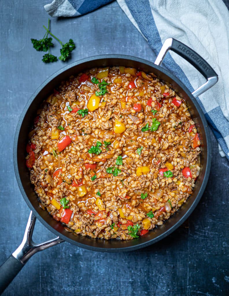 Photo of deconstructed stuffed pepper with pearl barley in a pan on the table