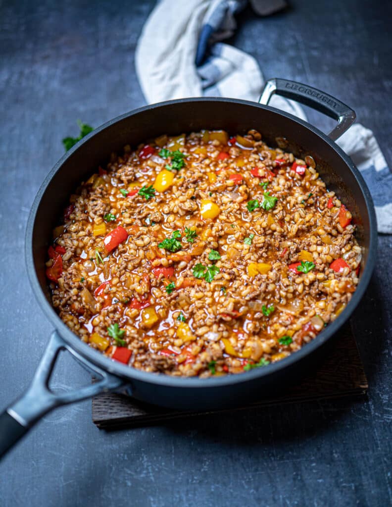 Photo of deconstructed stuffed pepper with pearl barley in a pan on the table
