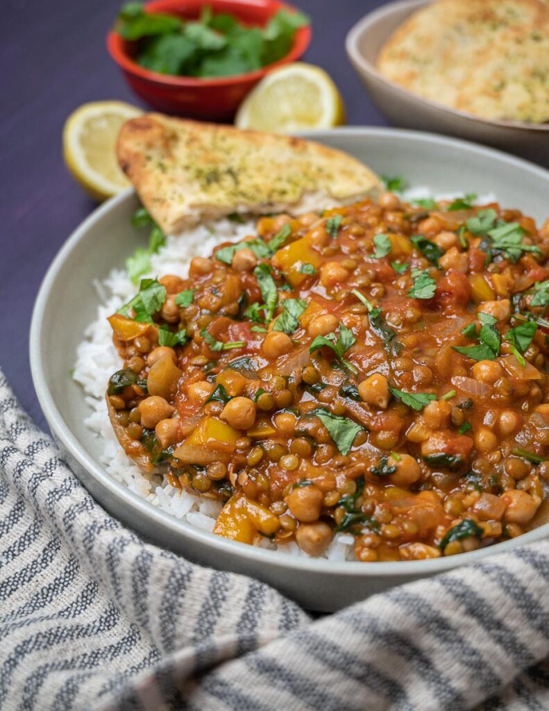 A close up photo of a bowl of lentil and chickpeas curry with naan bread