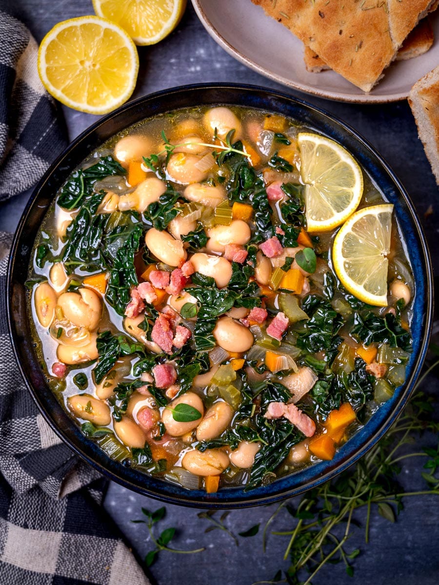 A bowl of butter beans soup with lemons and bread on the side