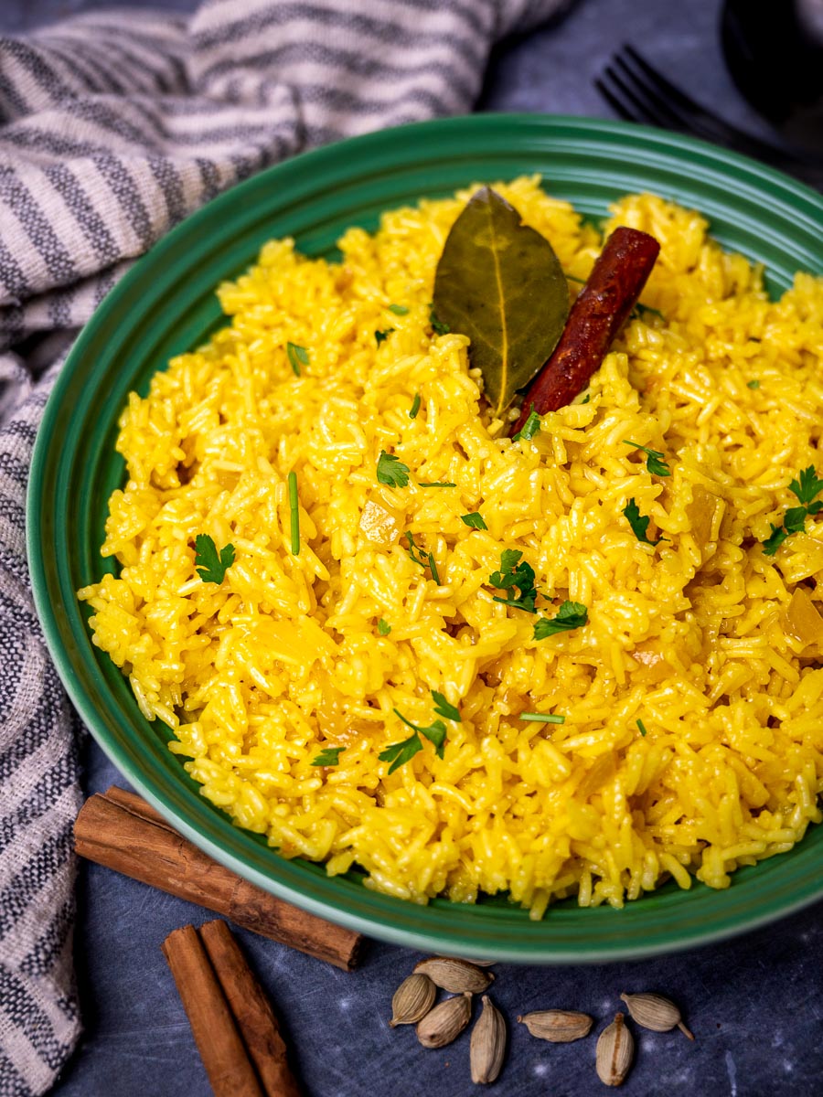 A bowl of pilau rice with cinnamon sticks and cardamom on the side
