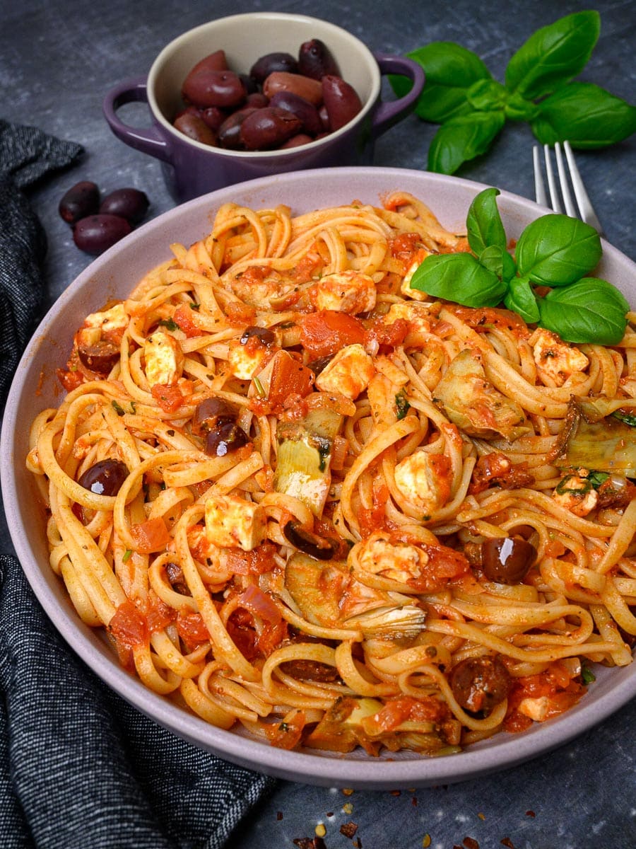 A bowl of vegetarian pasta with olives on the side