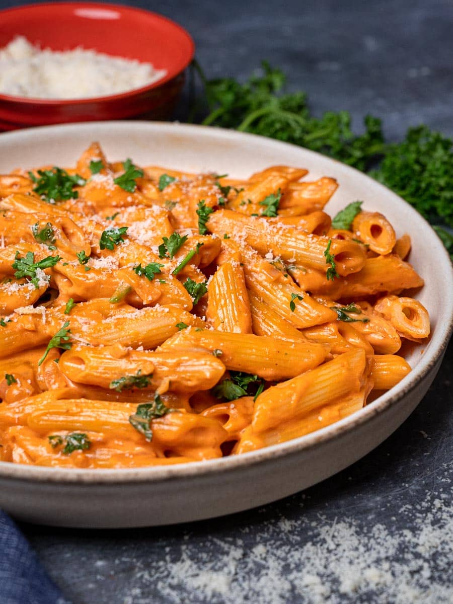 Close up photo of a bowl of pink sauce pasta with parmesan on the side