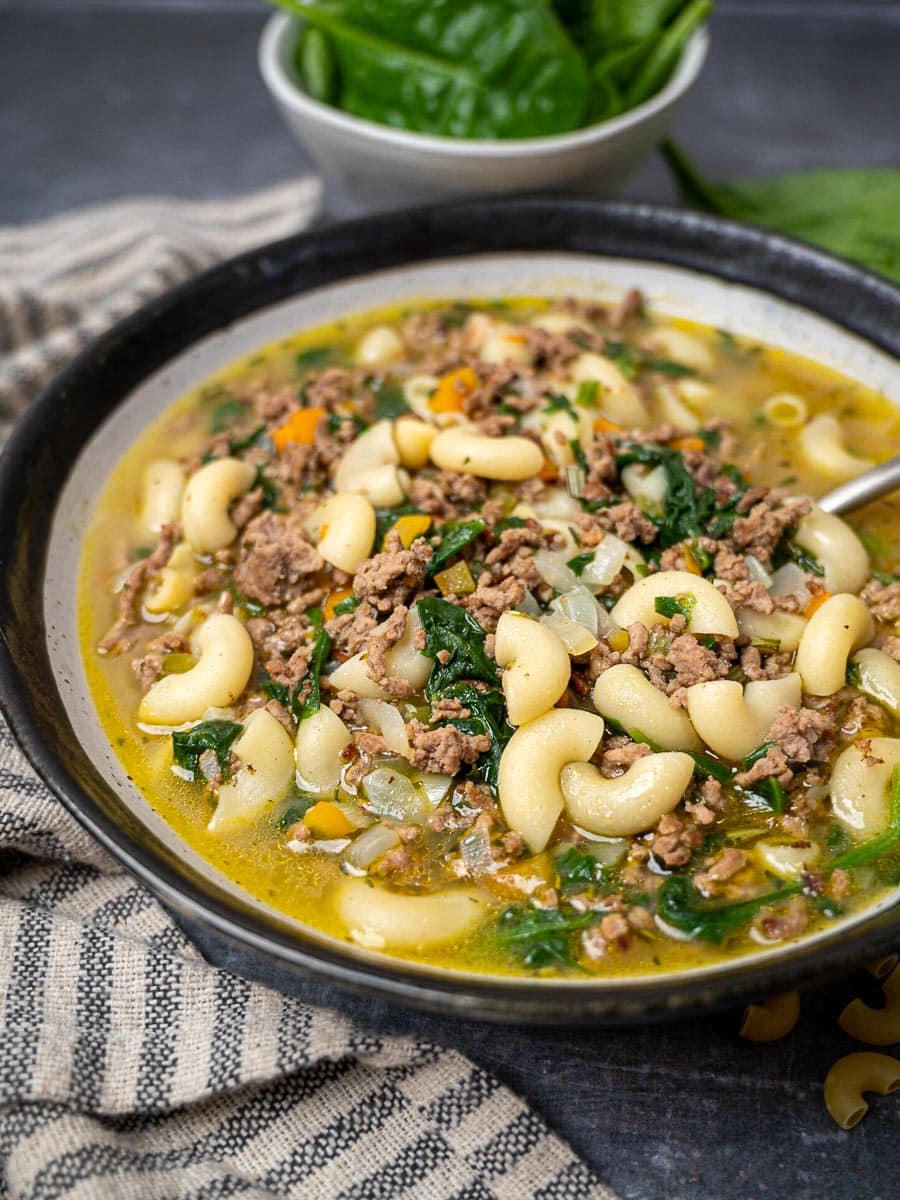 A bowl of pasta soup with meat and spinach