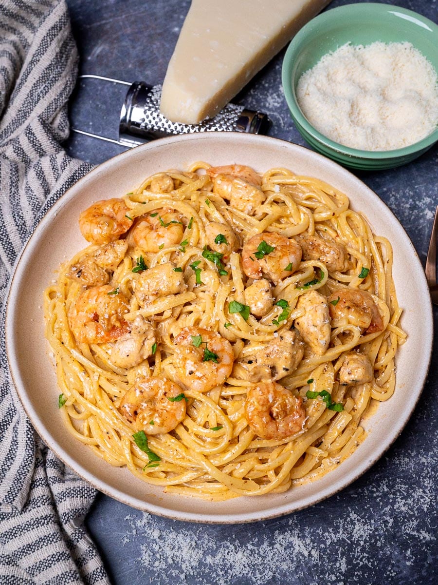 A bowl of creamy Cajun chicken pasta with parmesan on the side