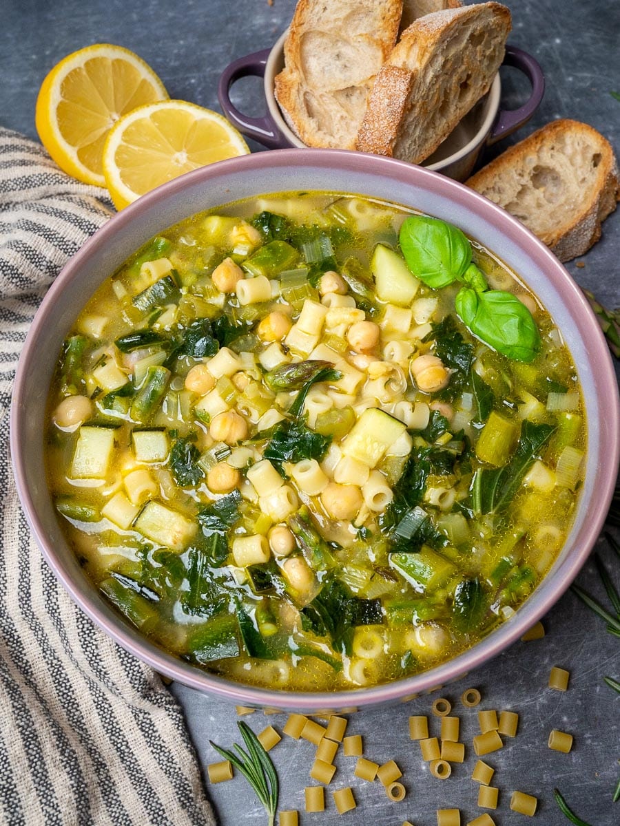 A bowl of spring minestrone soup with bread and lemon on the side