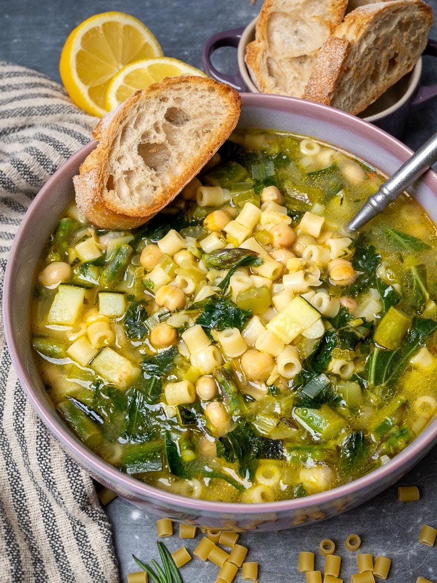A bowl of minestrone with vegetables and a slice of bread