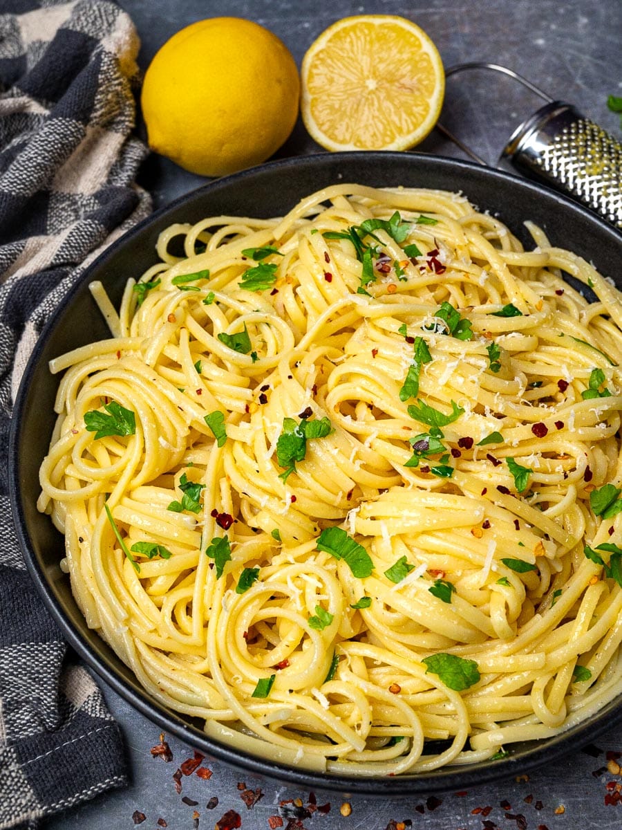 A bowl of lemon butter garlic pasta with lemons on the side
