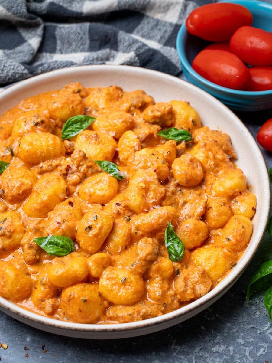 A plate of creamy gnocchi with tomatoes on the side