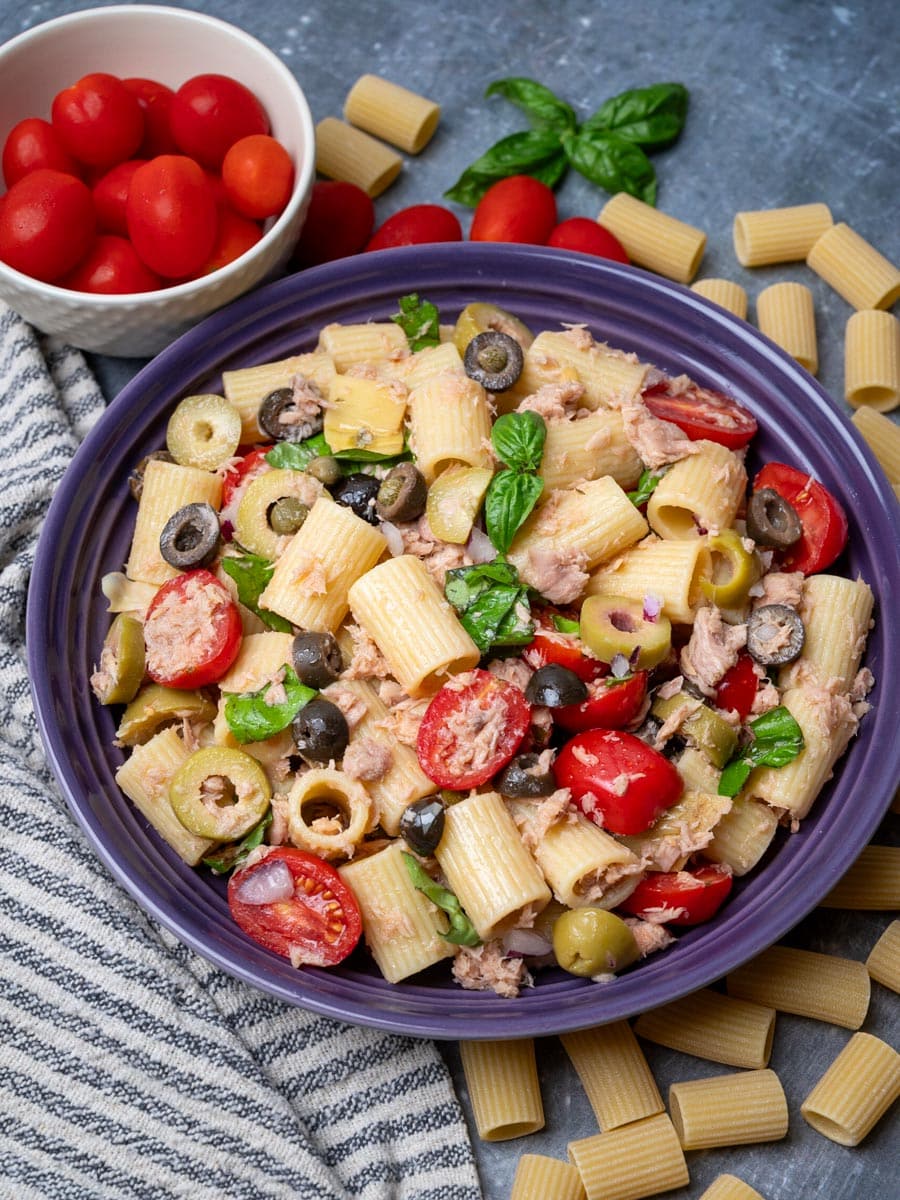 A bowl of pasta salad with tuna, olives, tomatoes and capers