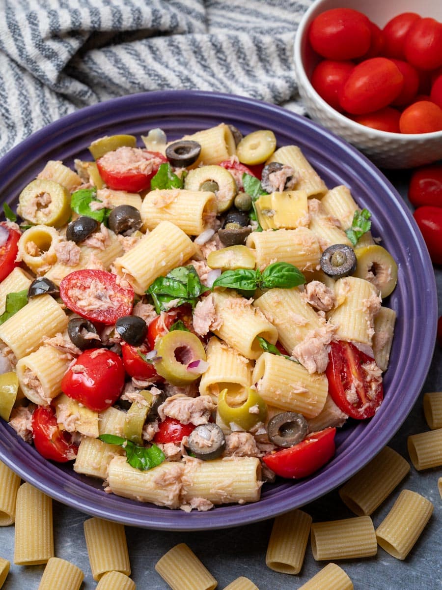 A bowl of pasta salad with tomatoes on the side