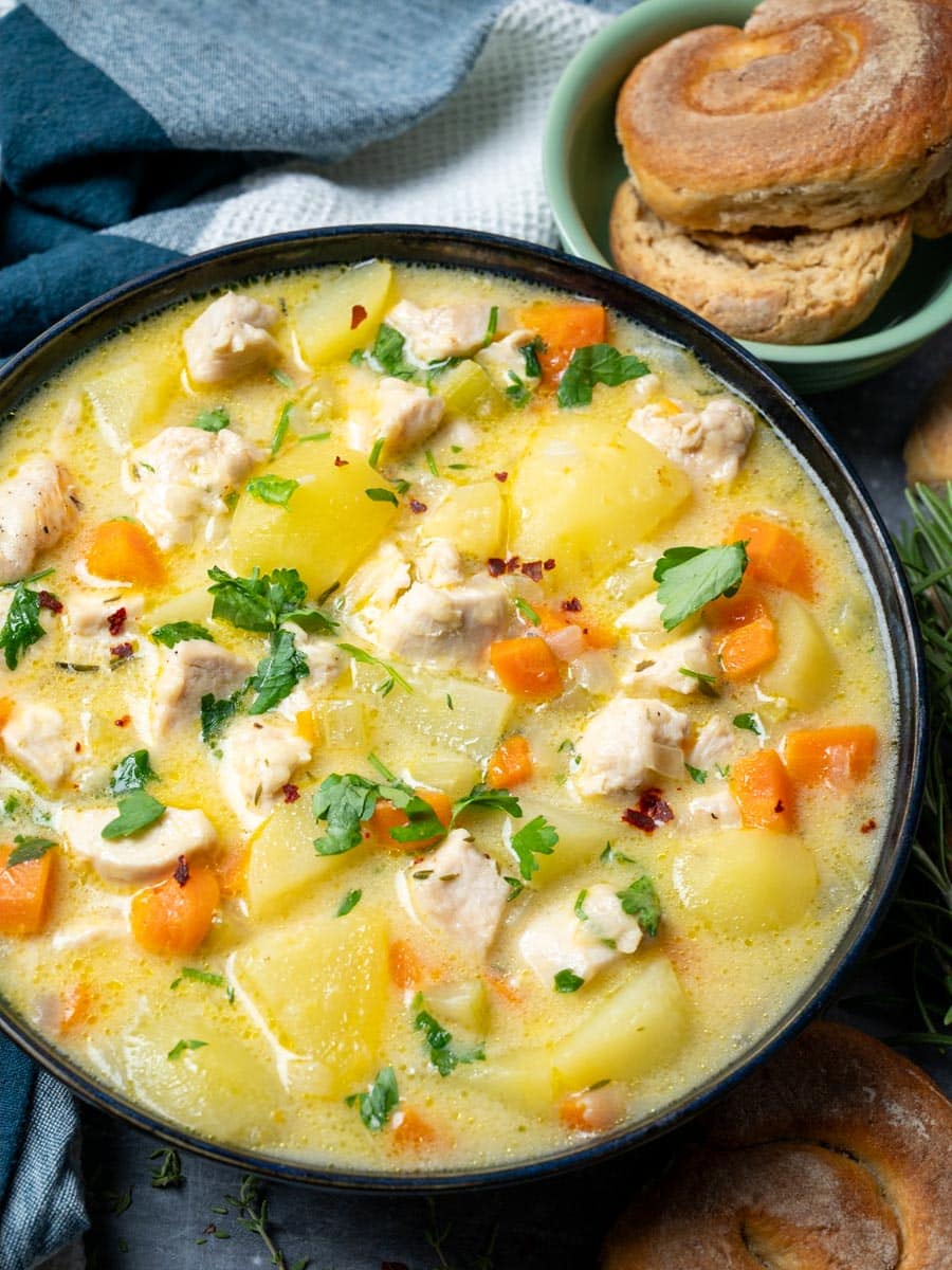 A close up photo of a bowl of soup with potatoes and pieces of chicken