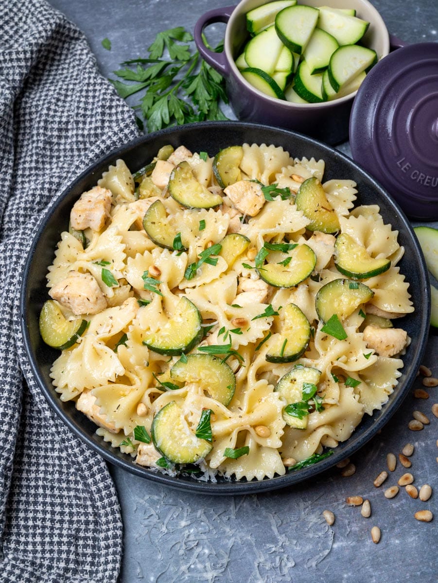 A photo of a bowl of pasta with fresh zucchini and pine nuts on the side