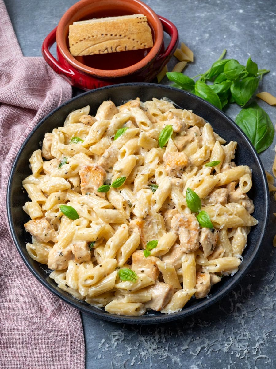 A bowl of creamy chicken pasta with parmesan on the side