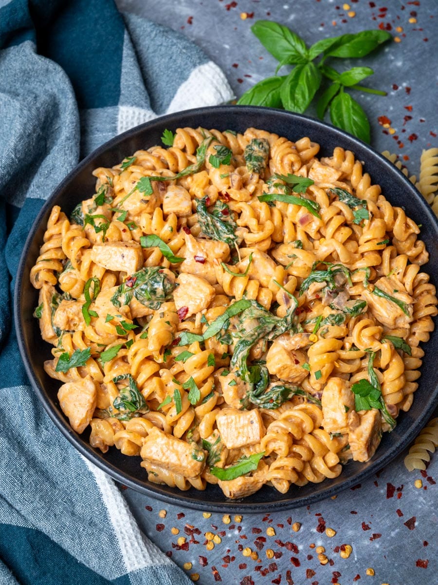 A bowl of pasta with chicken, spinach and fresh basil