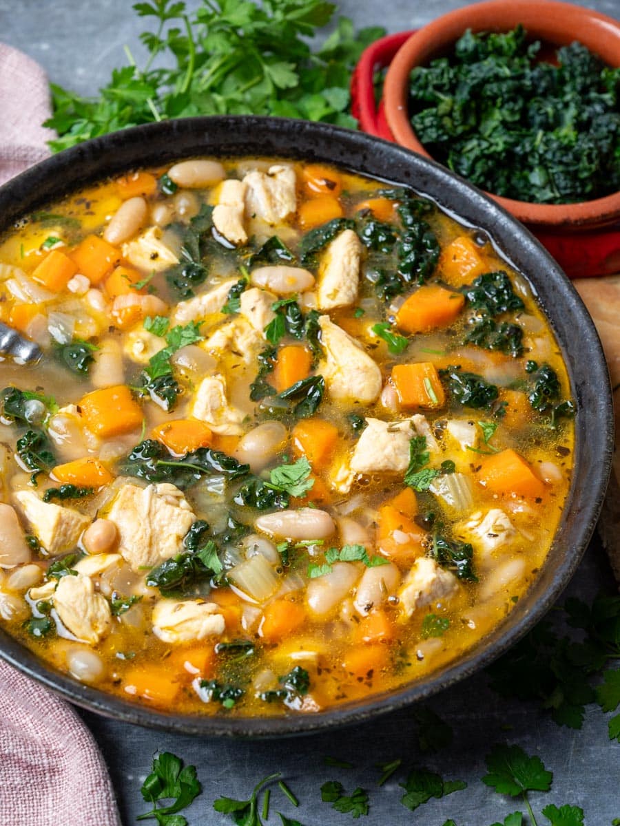 A bowl of chicken soup with kale and beans.