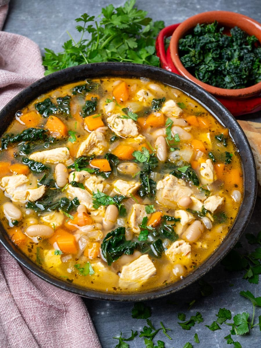 A bowl of chicken soup with kale on the side.