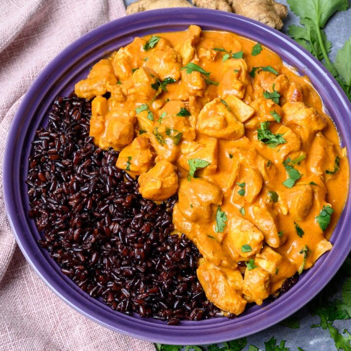 A bowl of butter chicken curry with black rice.