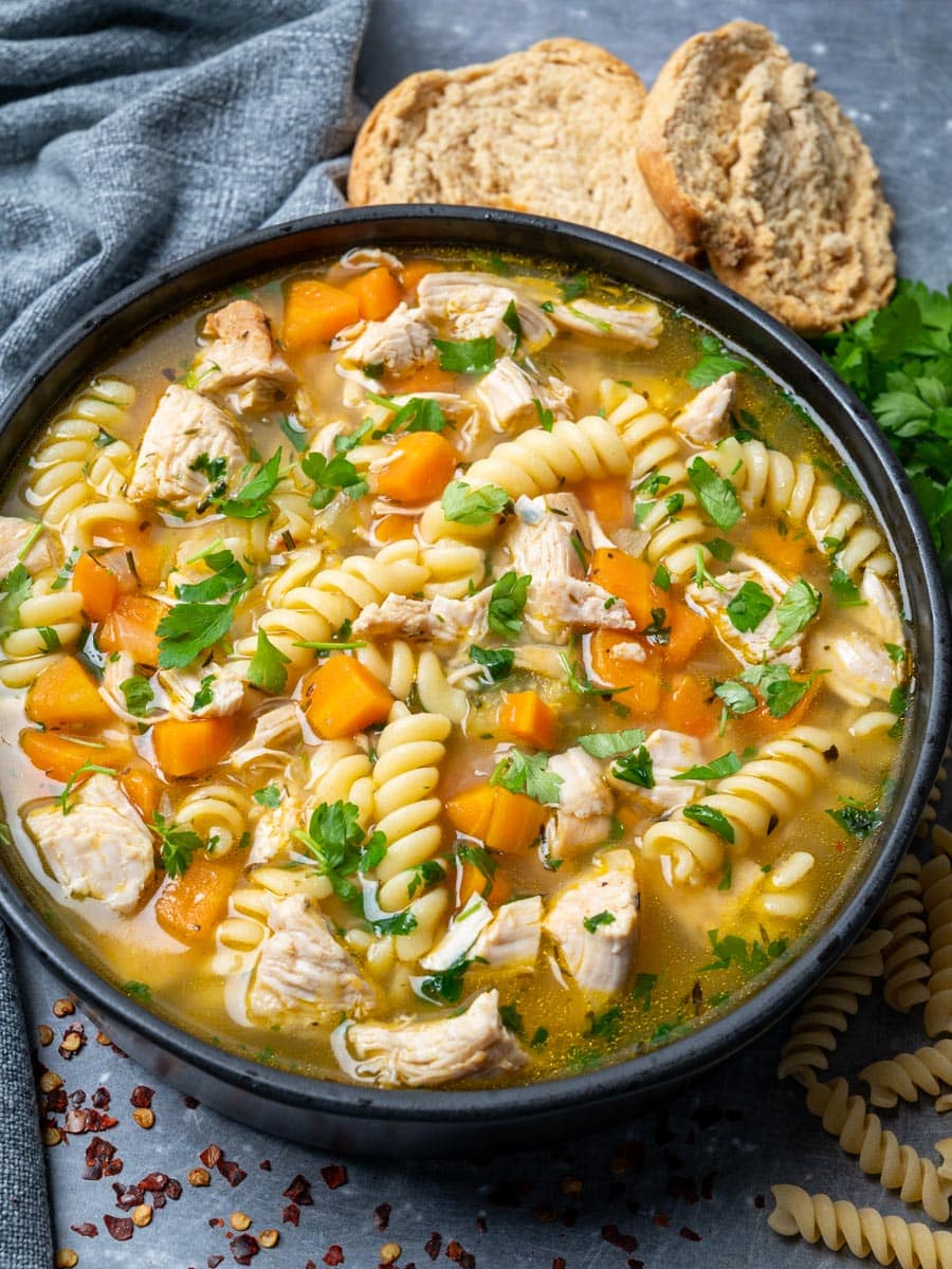 A bowl of turkey noodle soup with crusty bread on the side.