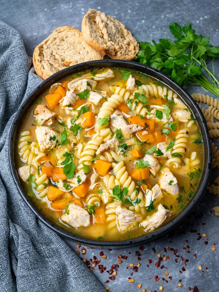 A black bowl of turkey soup with boodles and veggies.