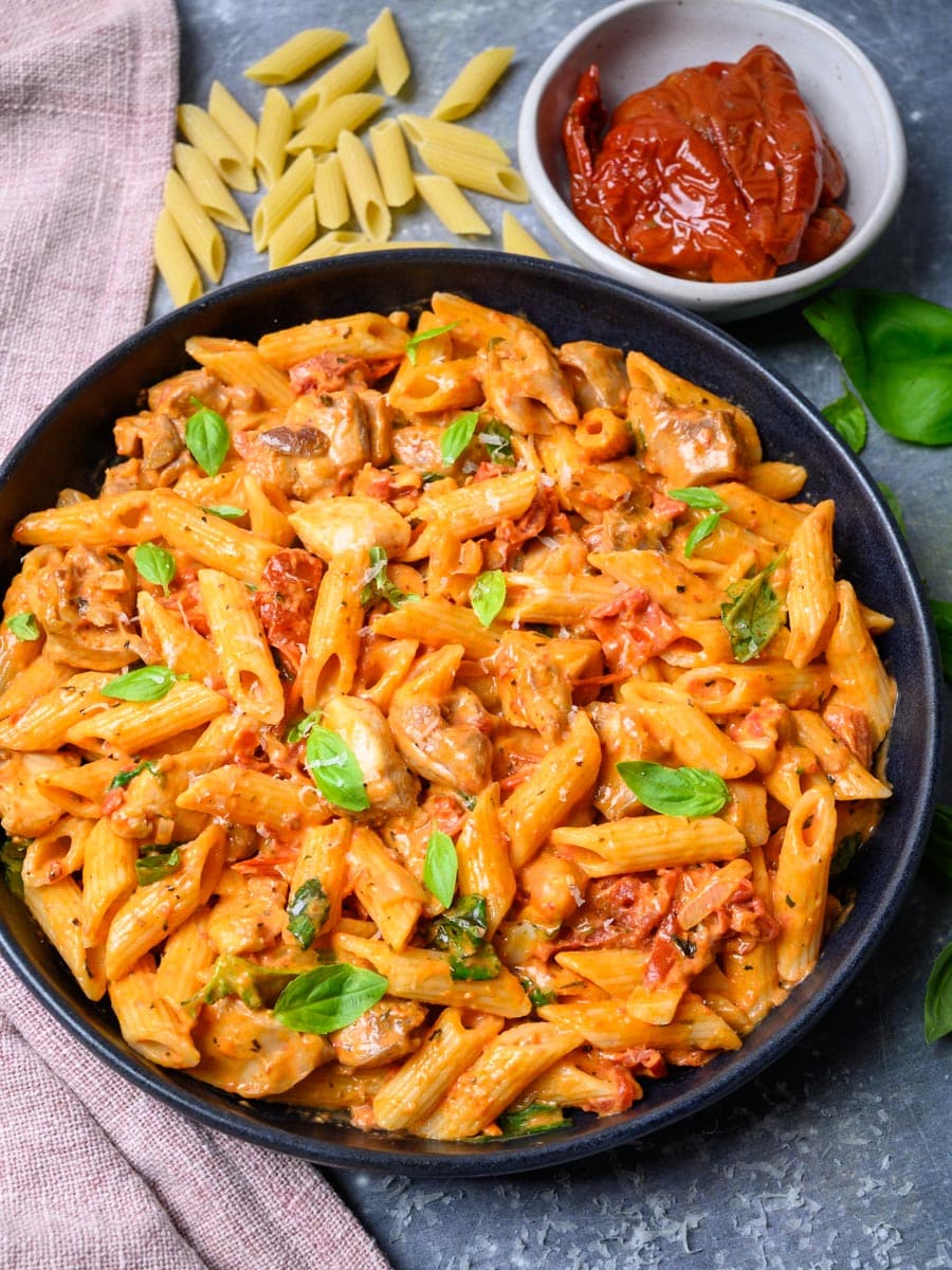 A pasta dish with sun dried tomatoes, chicken and basil.