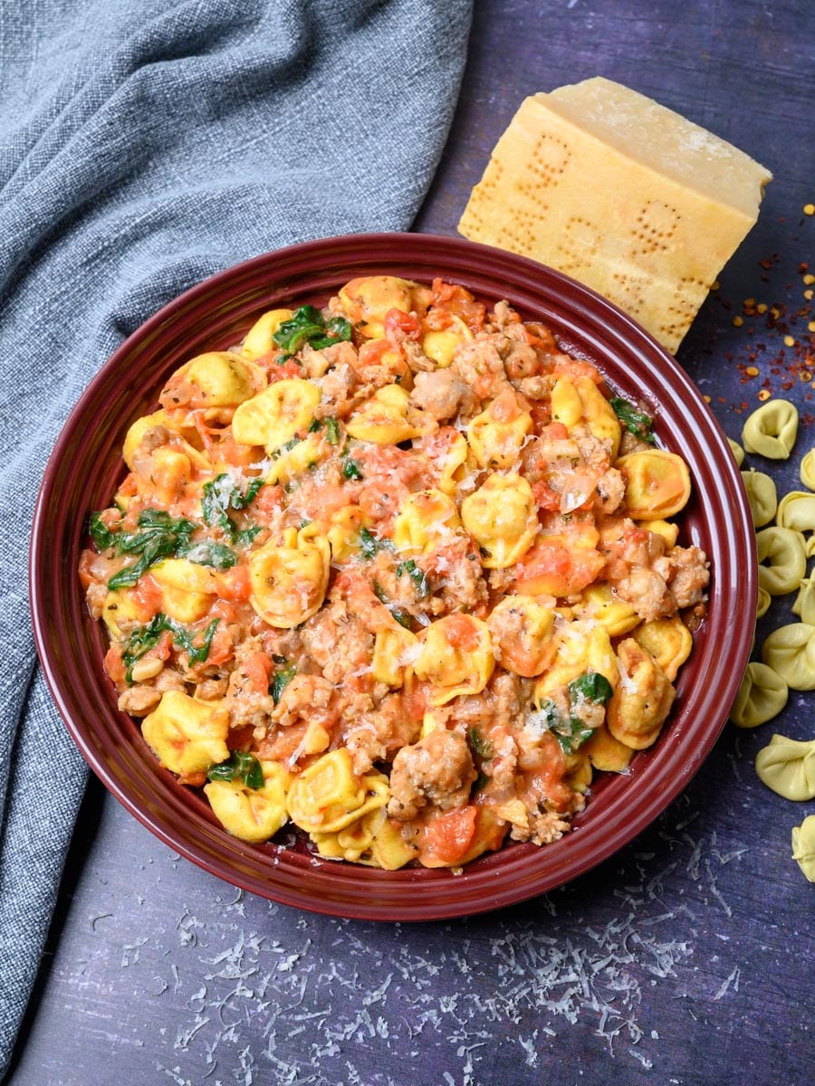 A bowl of tortellini with spinach, sausage and Parmesan.