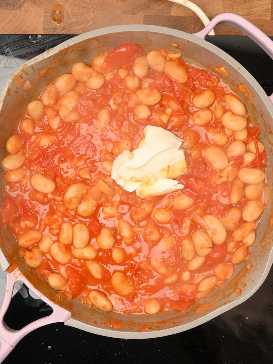 adding cream cheese to a tomato basil butter beans