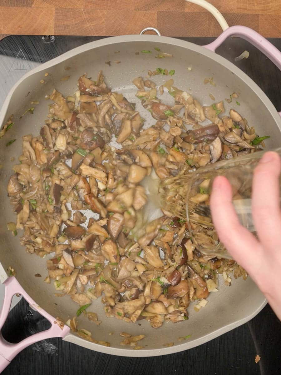 adding wine to a garlic mushroom pasta