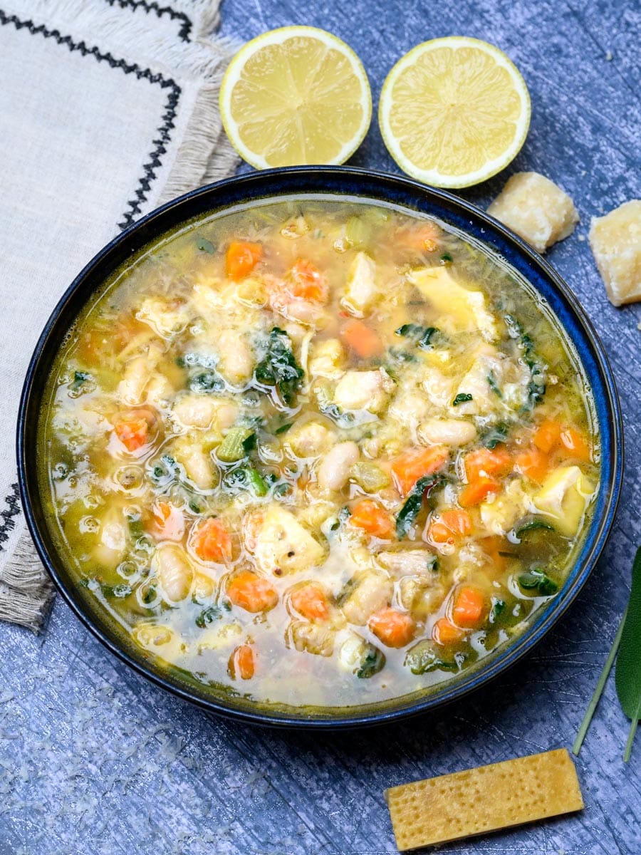 A bowl of chicken parmesan soup with lemons on the side