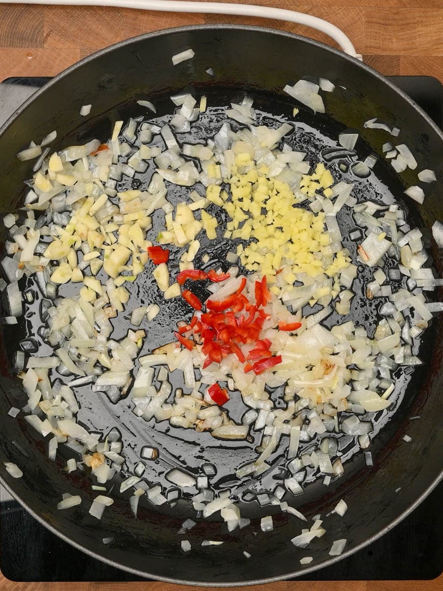 Diced onions cooking with garlic, ginger and red chili in a skillet