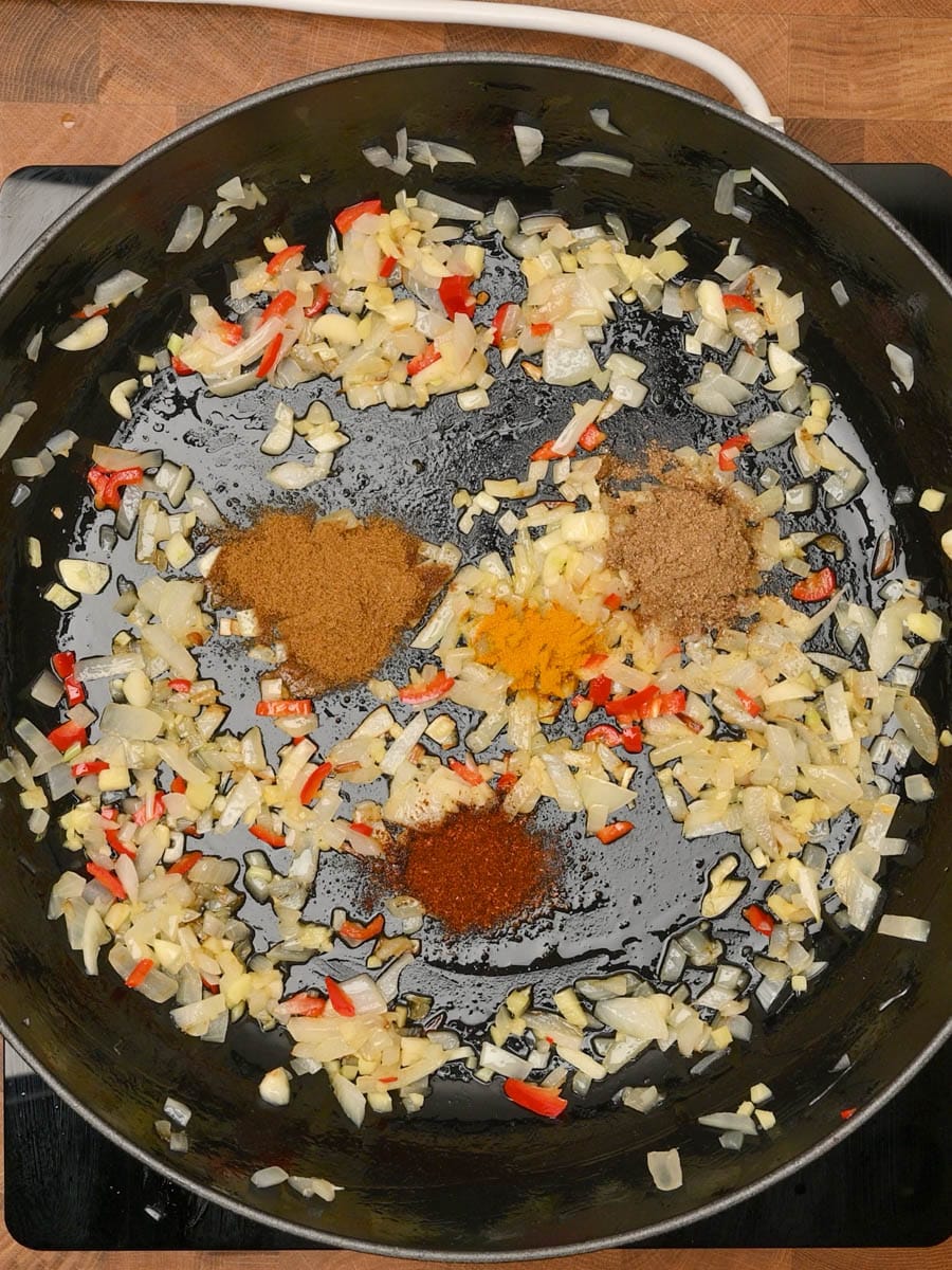 Curry powder, turmeric, and paprika added to sautéed onions and garlic in a skillet