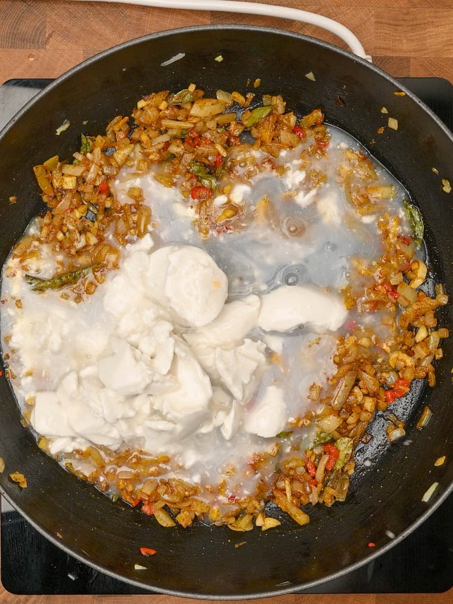 Coconut milk being stirred into a spiced onion and tomato base in a skillet