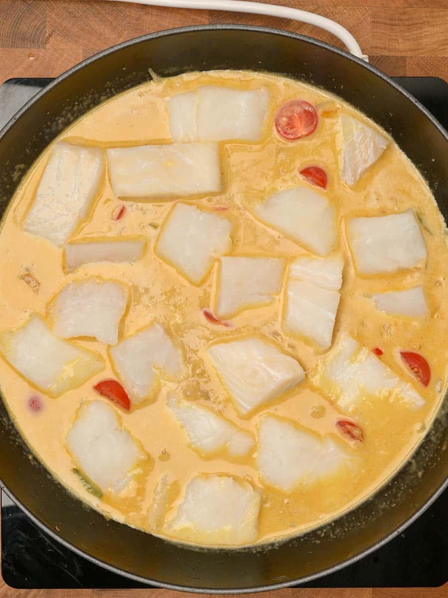 White fish fillets simmering in a golden, spiced coconut sauce with cherry tomatoes