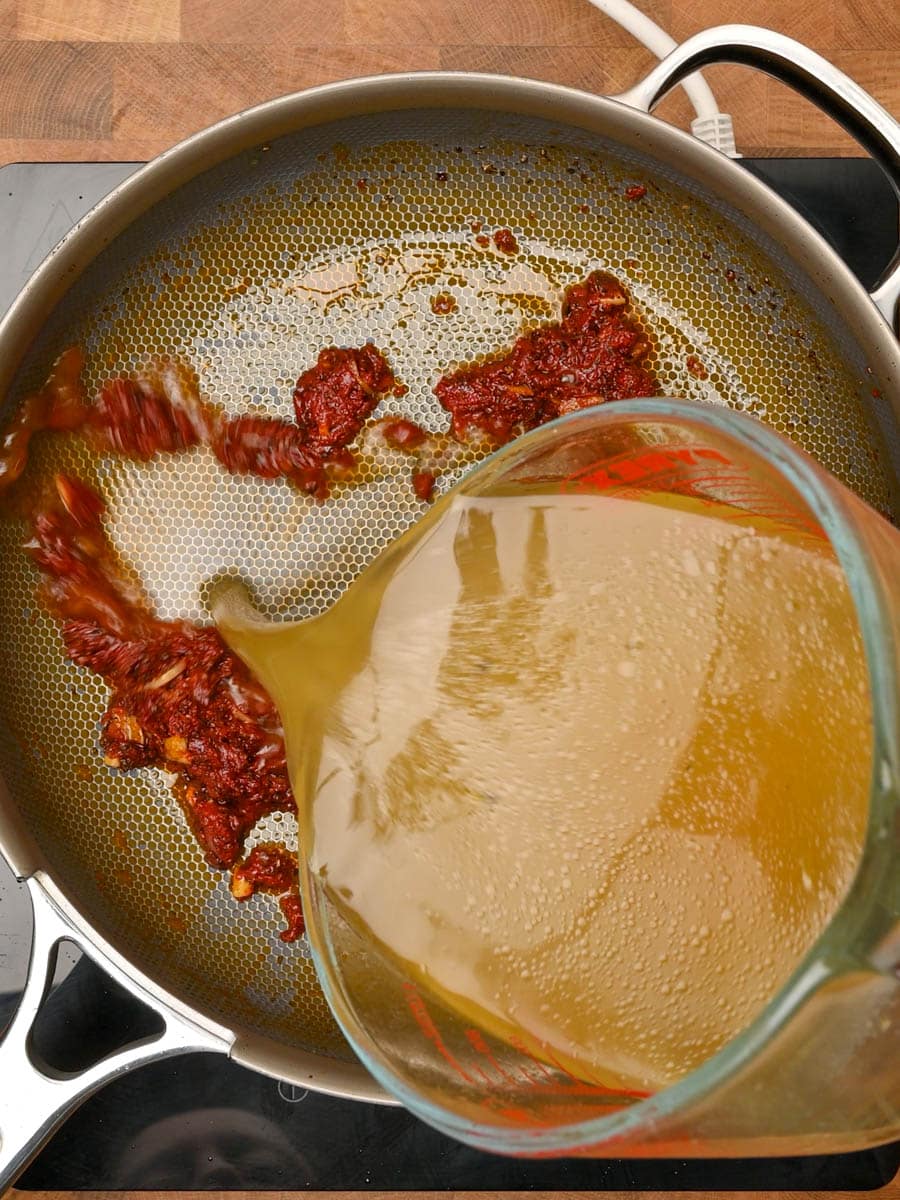 adding stock to a creamy tomato orzo