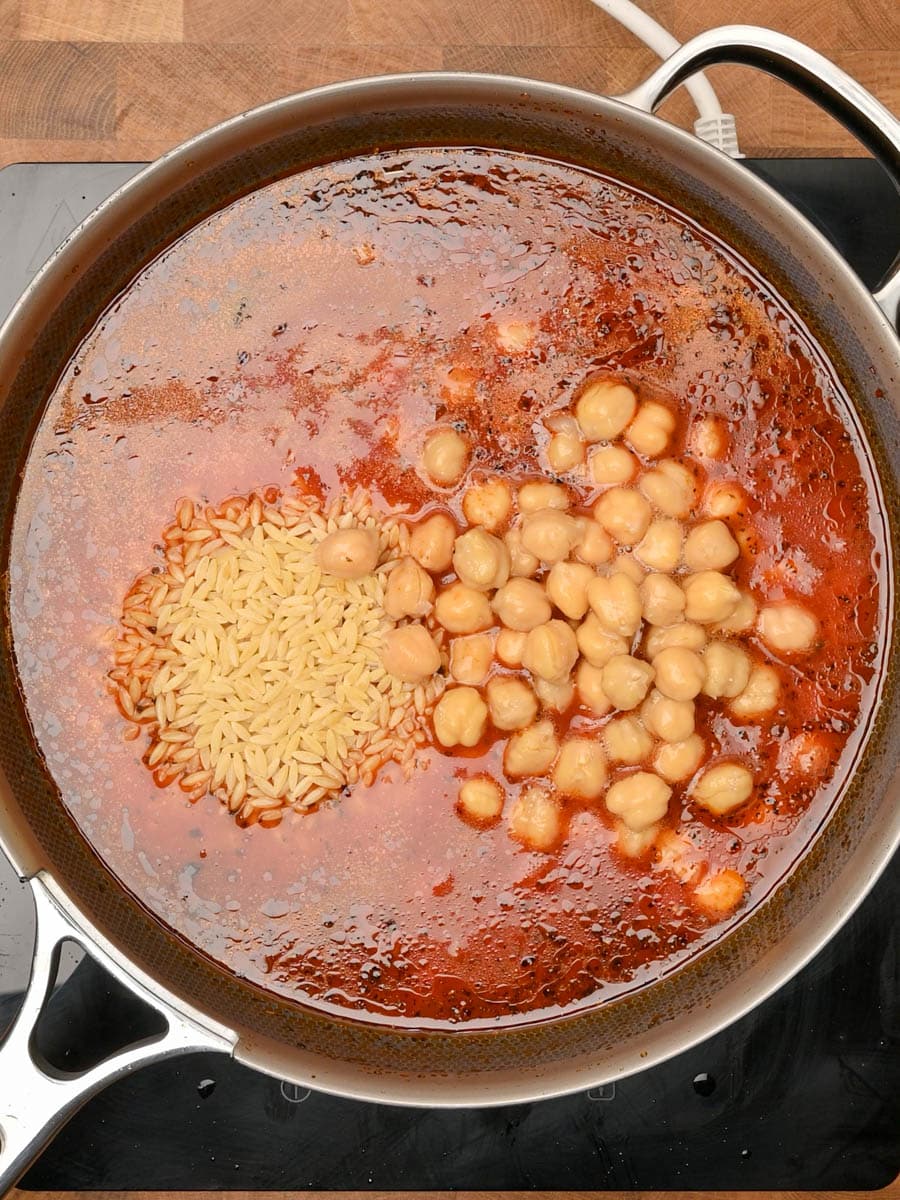 adding chickpeas to a creamy tomato orzo