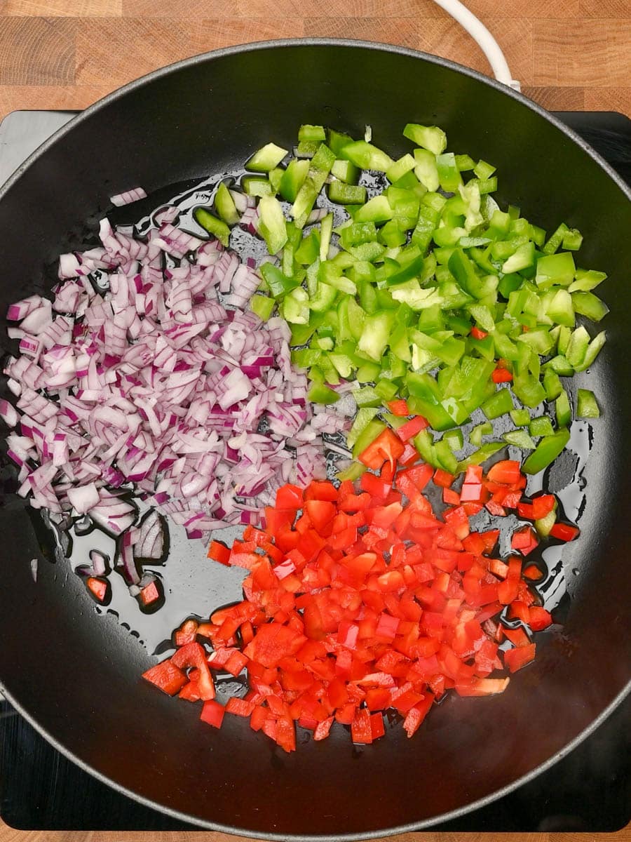 Adding red onion and peppers to a skillet with olive oil