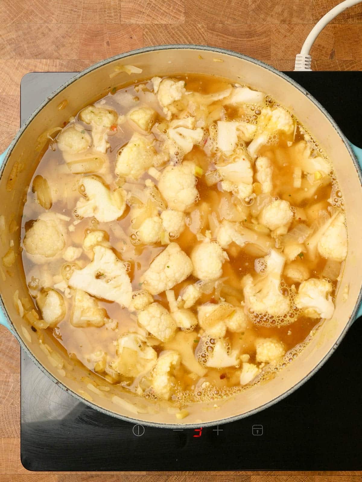 Adding stock to a cauliflower chicken soup.
