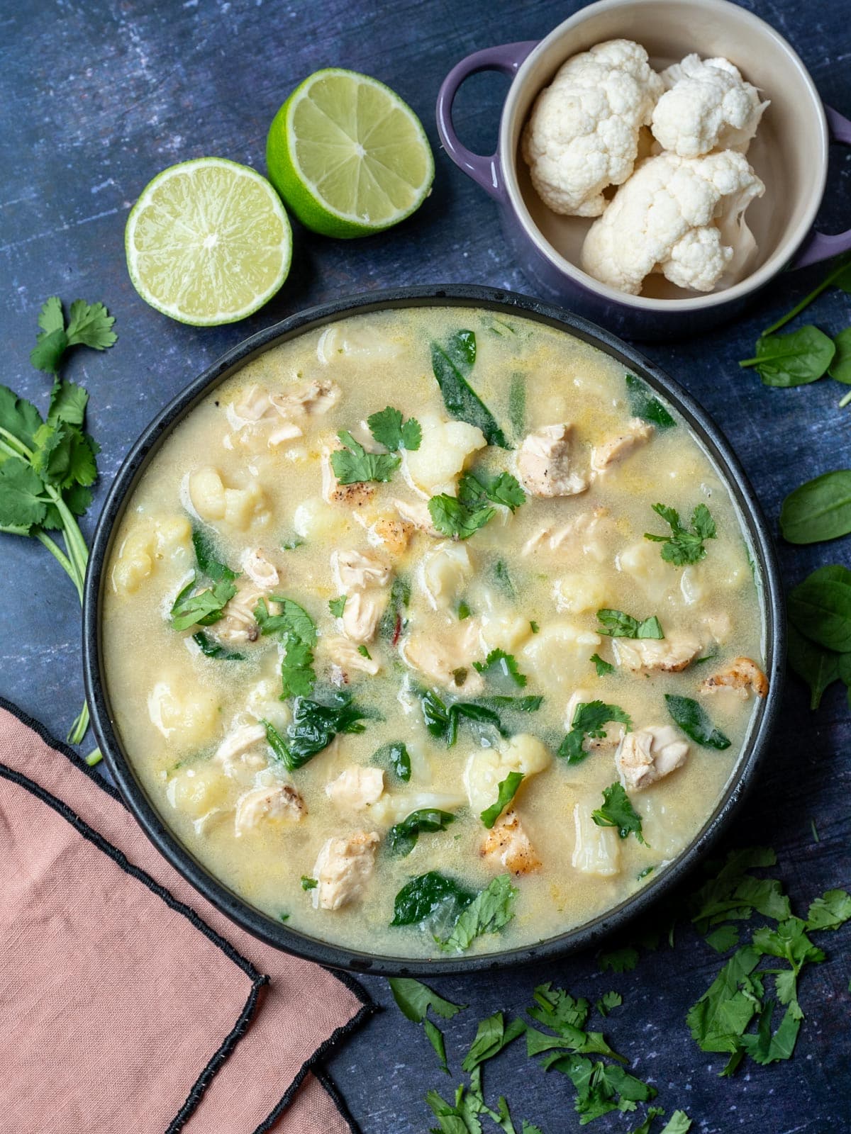 A bowl of cauliflower chicken soup with potatoes and limes.