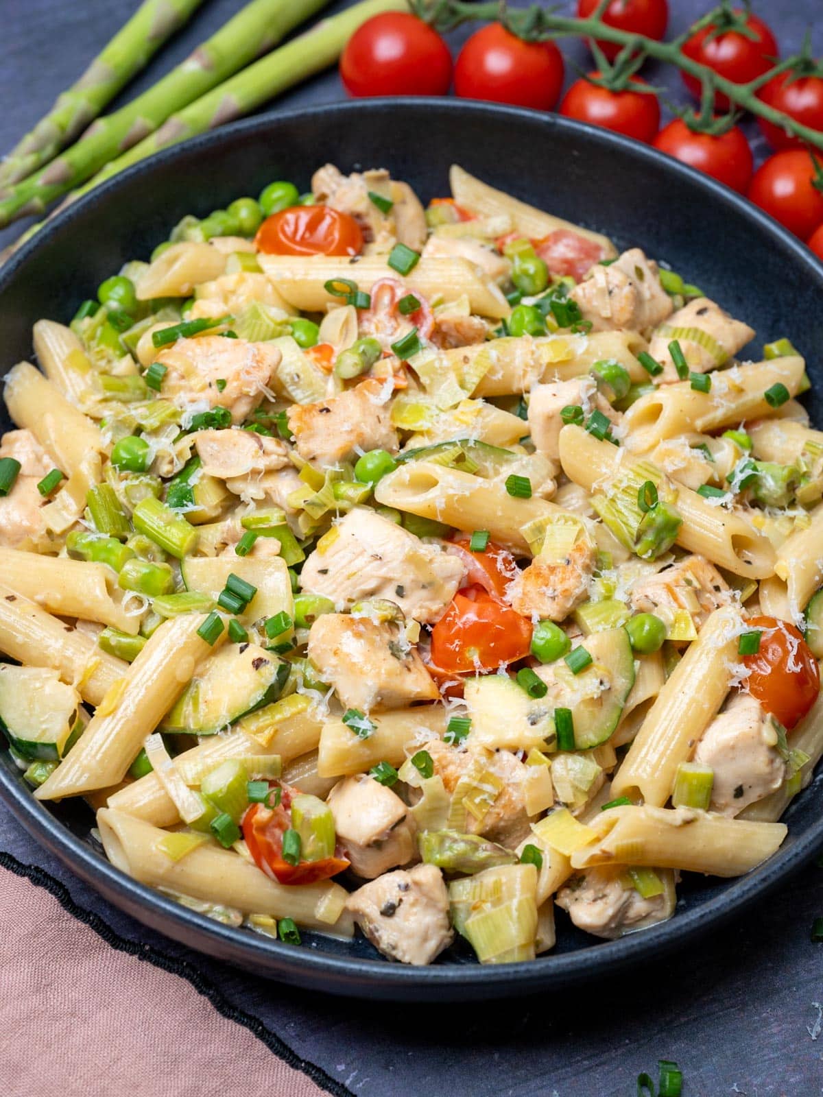 Close up photo of Chicken Pasta Primavera with tomatoes and asparagus on the side