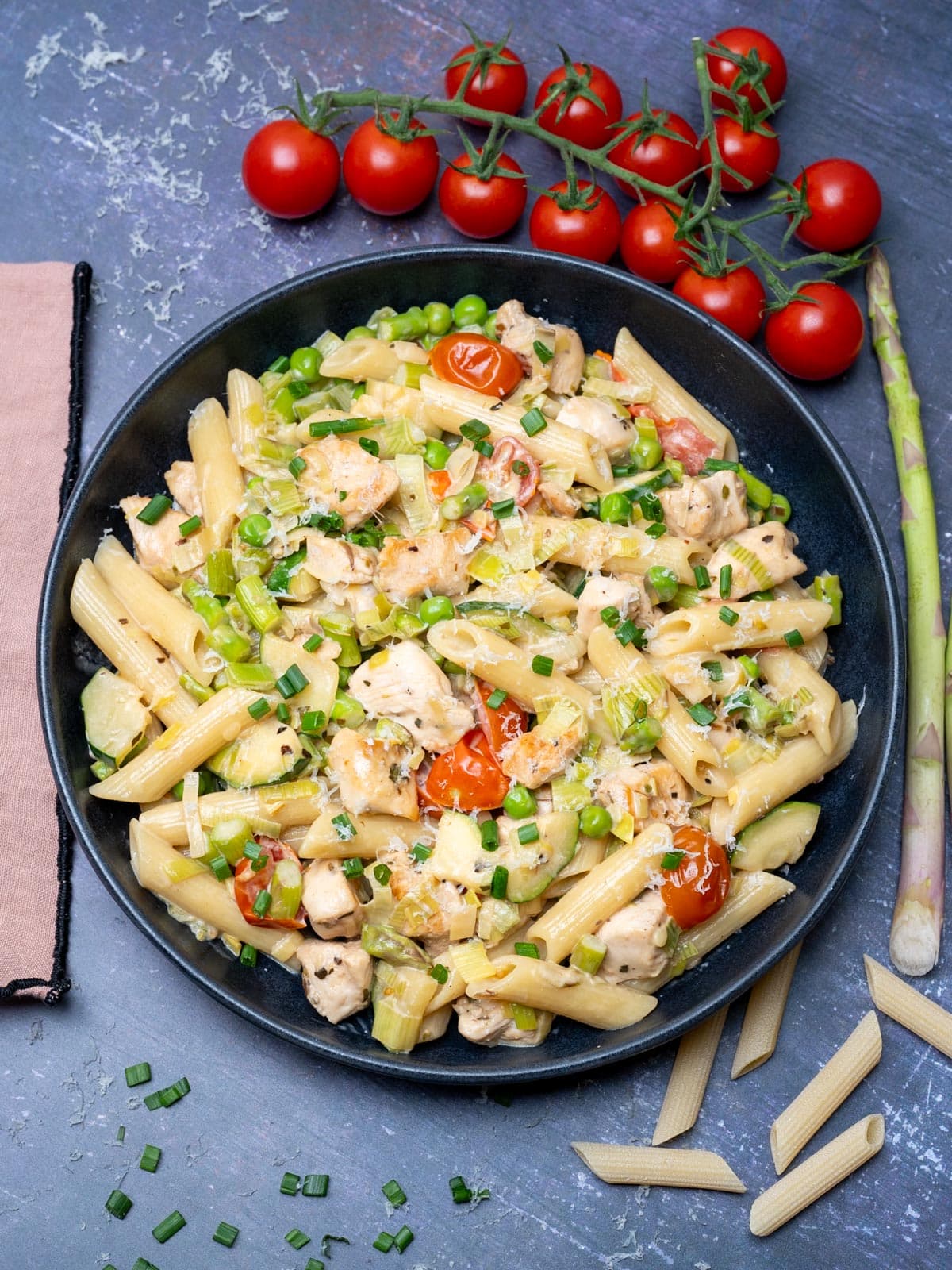 A bowl of penne with chicken, peas, tomatoes and asparagus
