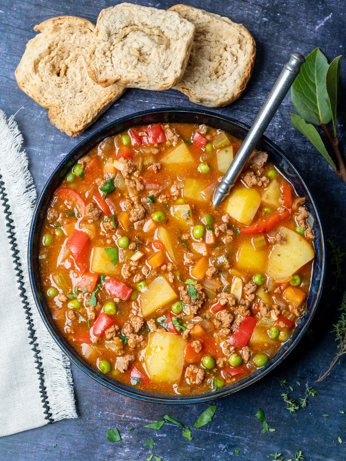 a bowl of stew with bread and thyme on the side