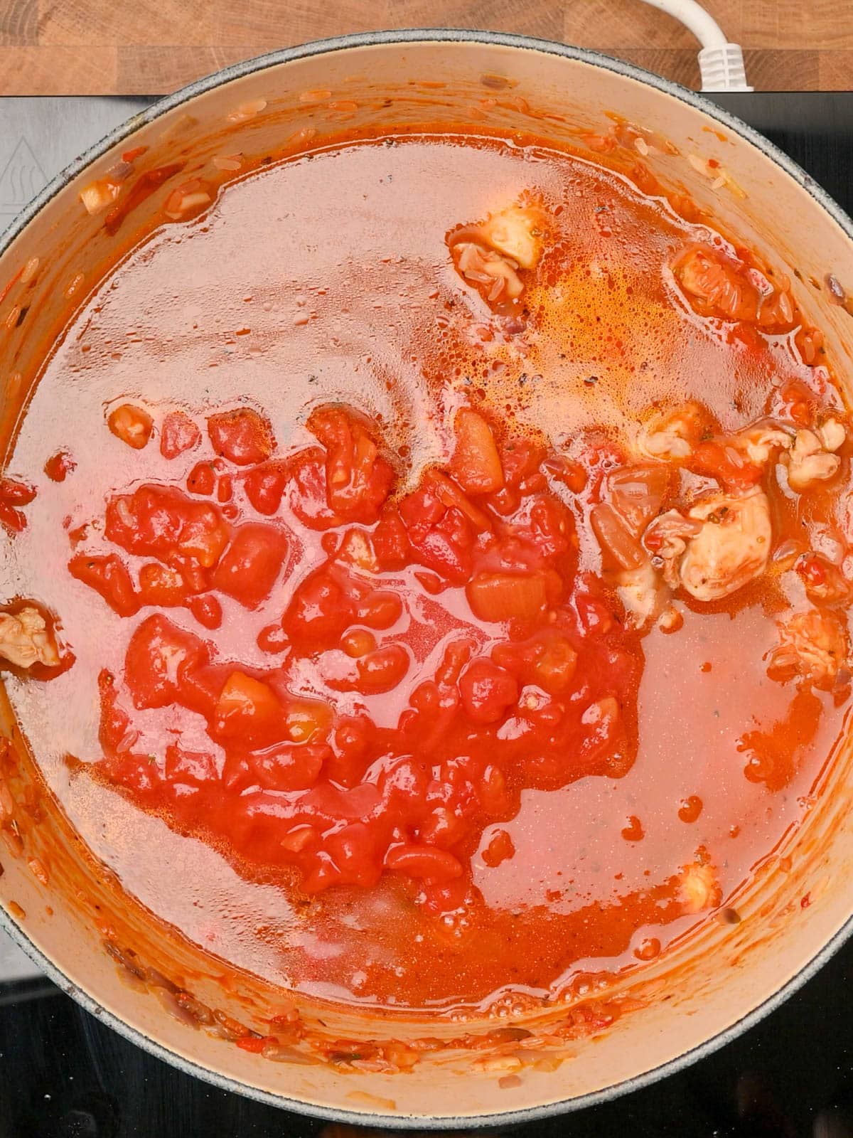 adding stock and chopped tomatoes to the chicken and chorizo rice