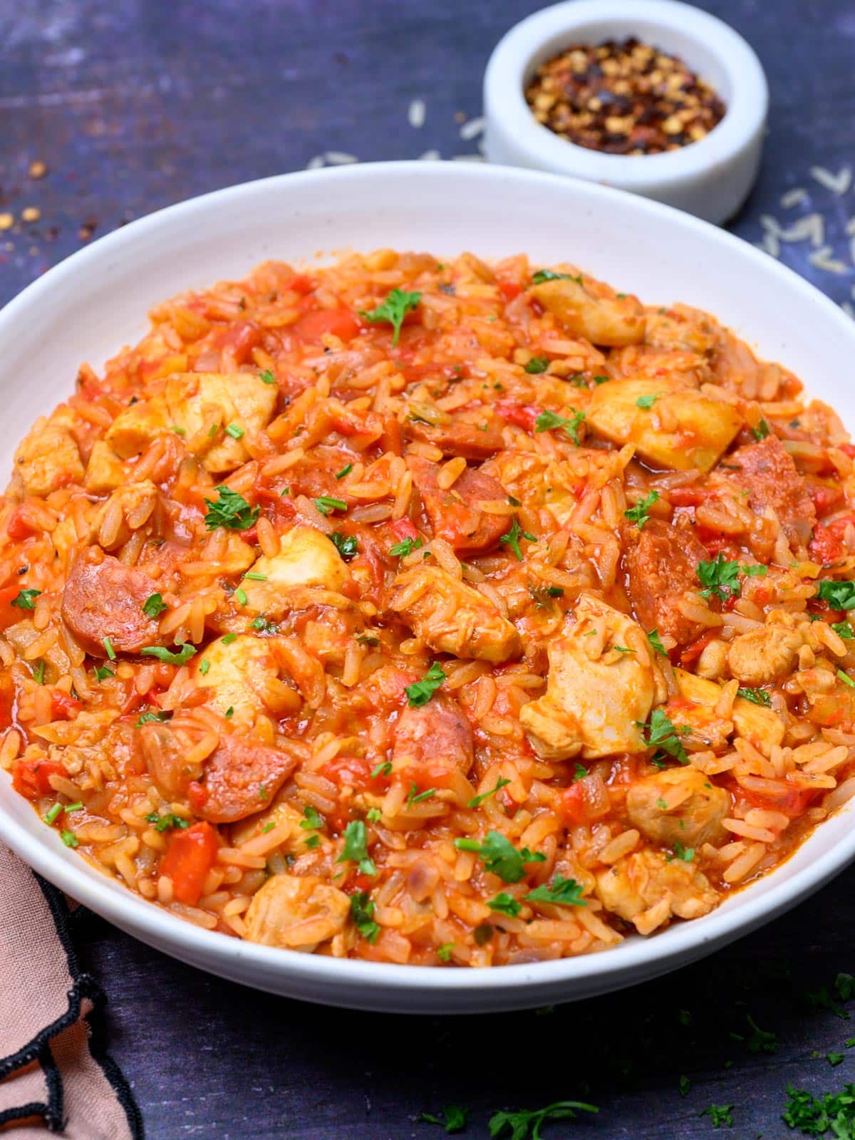 close up photo of a plate with rice, sausage and chili flakes on the side