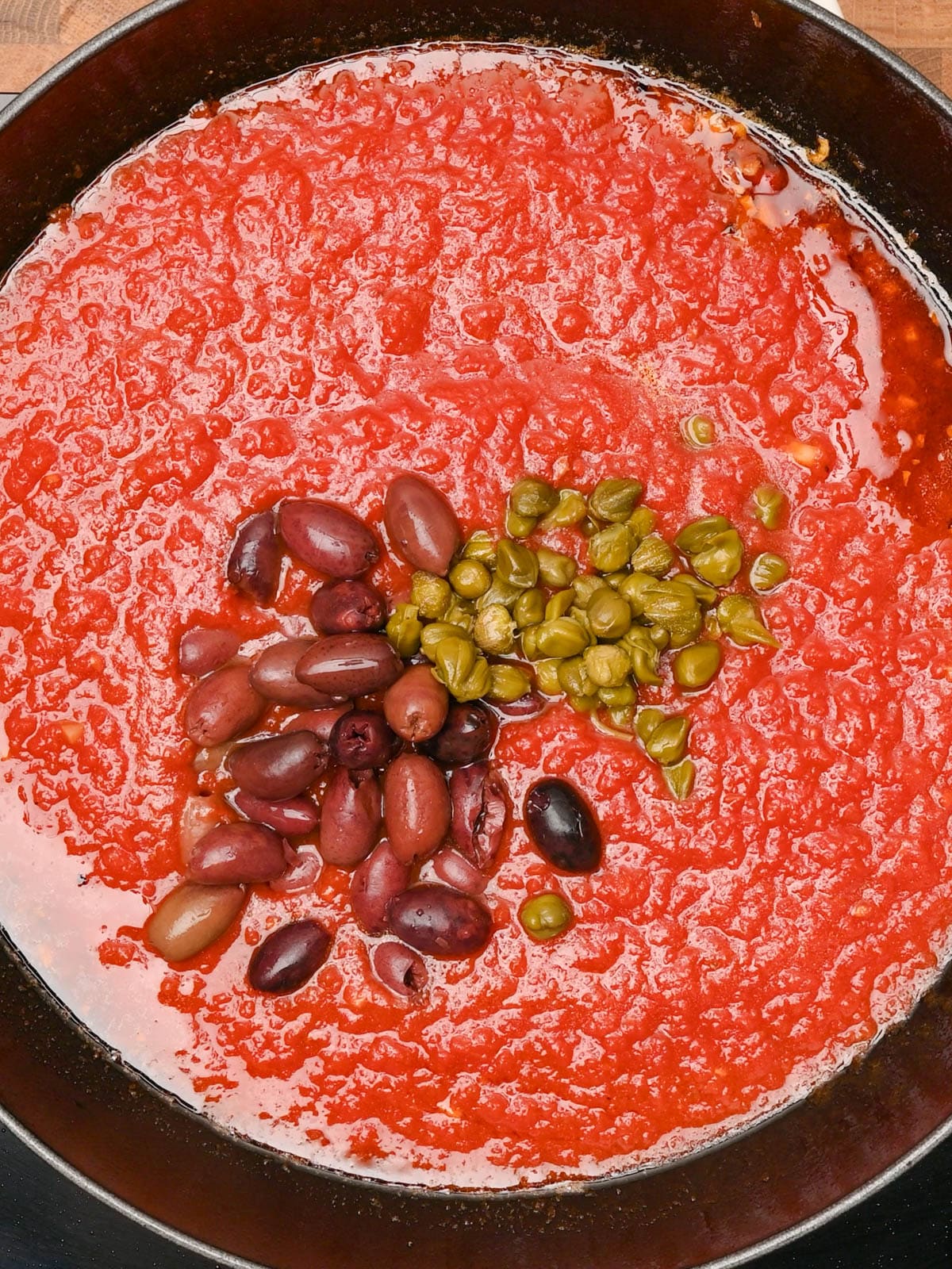 adding olives and capers to a red sauce
