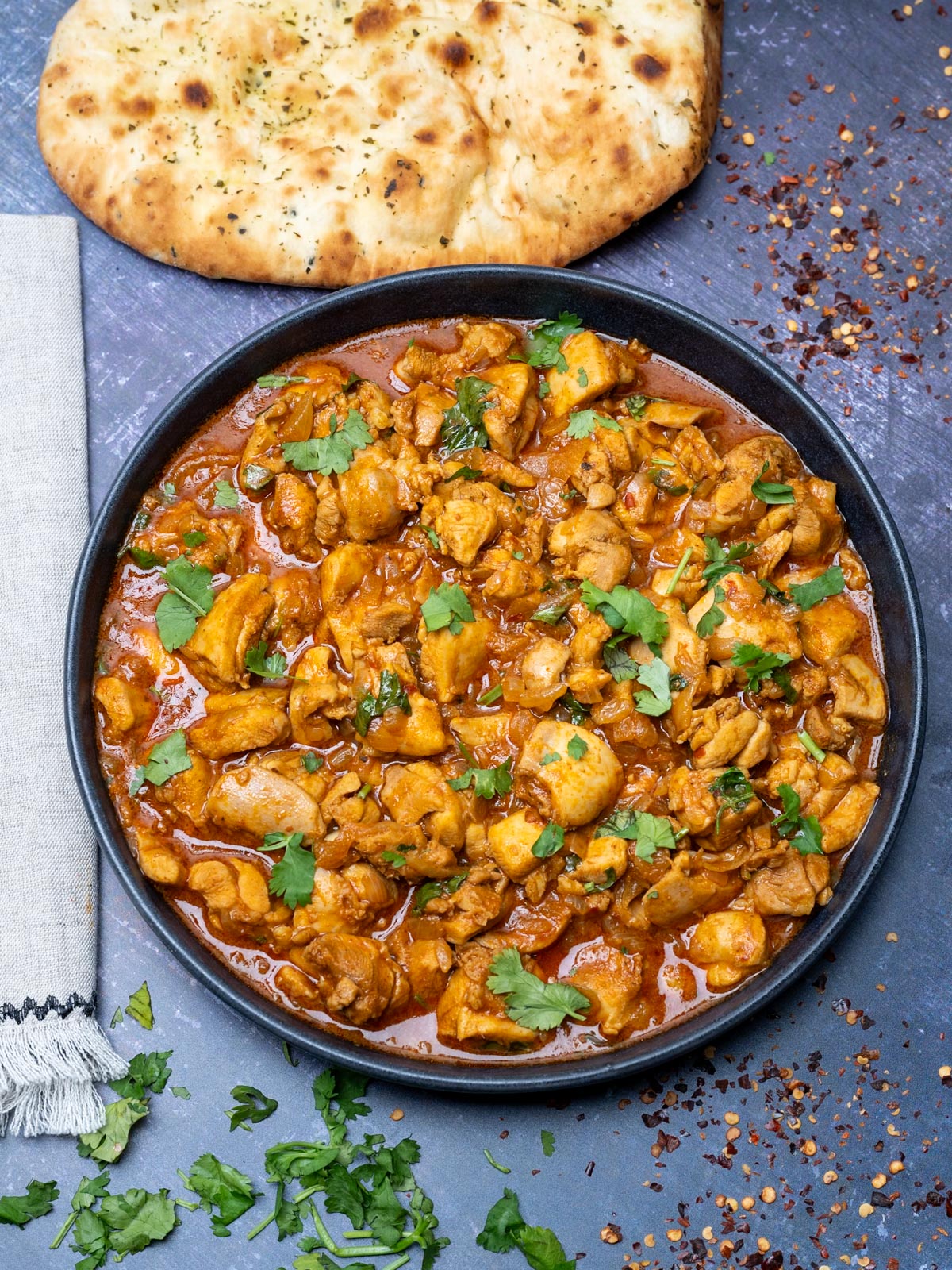 chicken vindaloo in a black bowl with a naan on the side