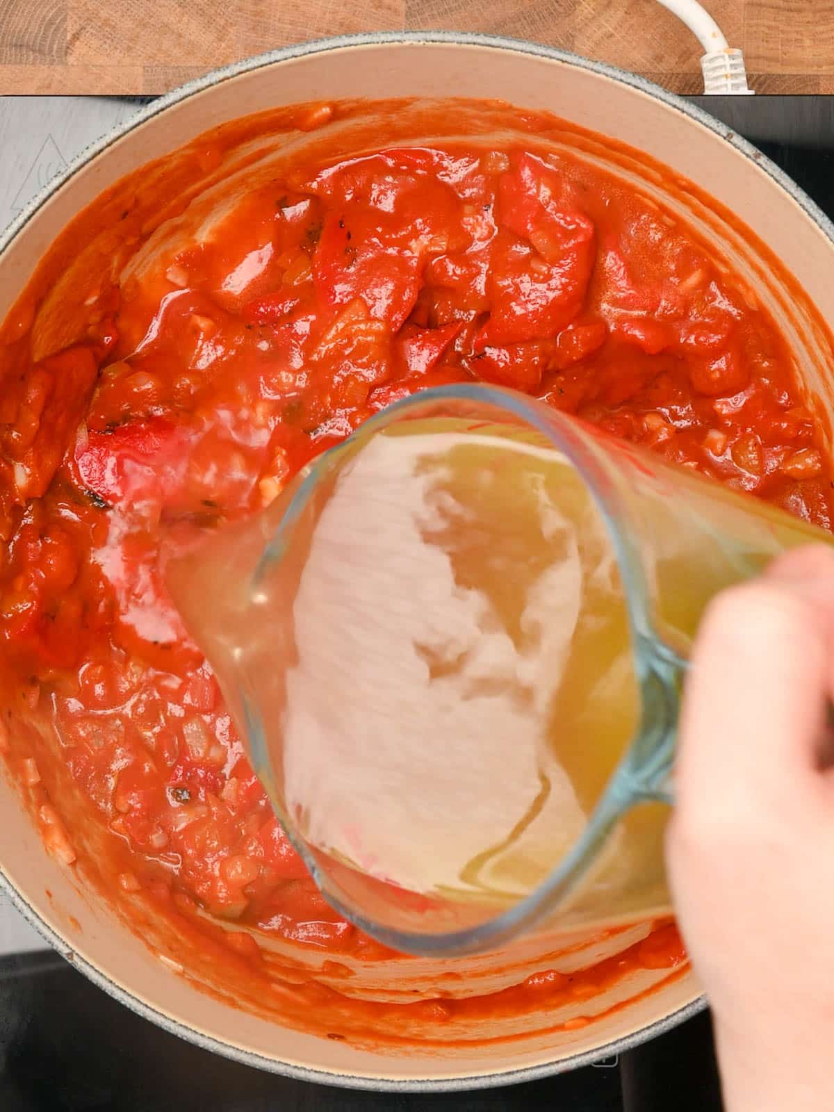 Pouring stock over the roasted peppers and tomato mixture.