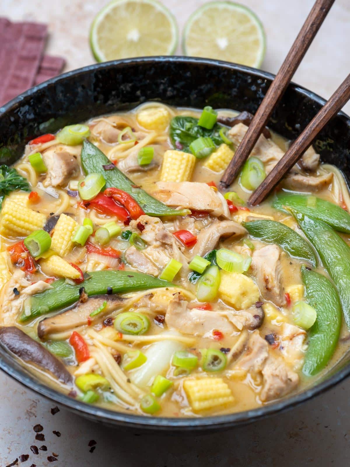 close up photo of a bowl of chicken, noodles, snap peas, baby corn and limes