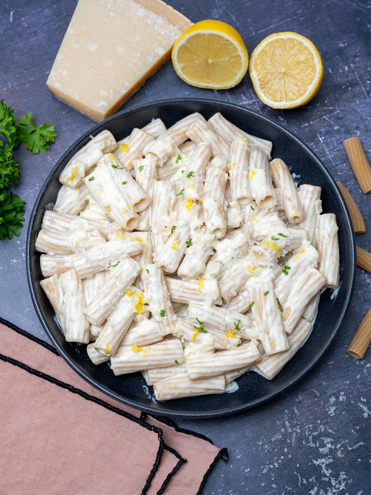 A black bowl of creamy lemon pasta with lemons and Parmesan on the side