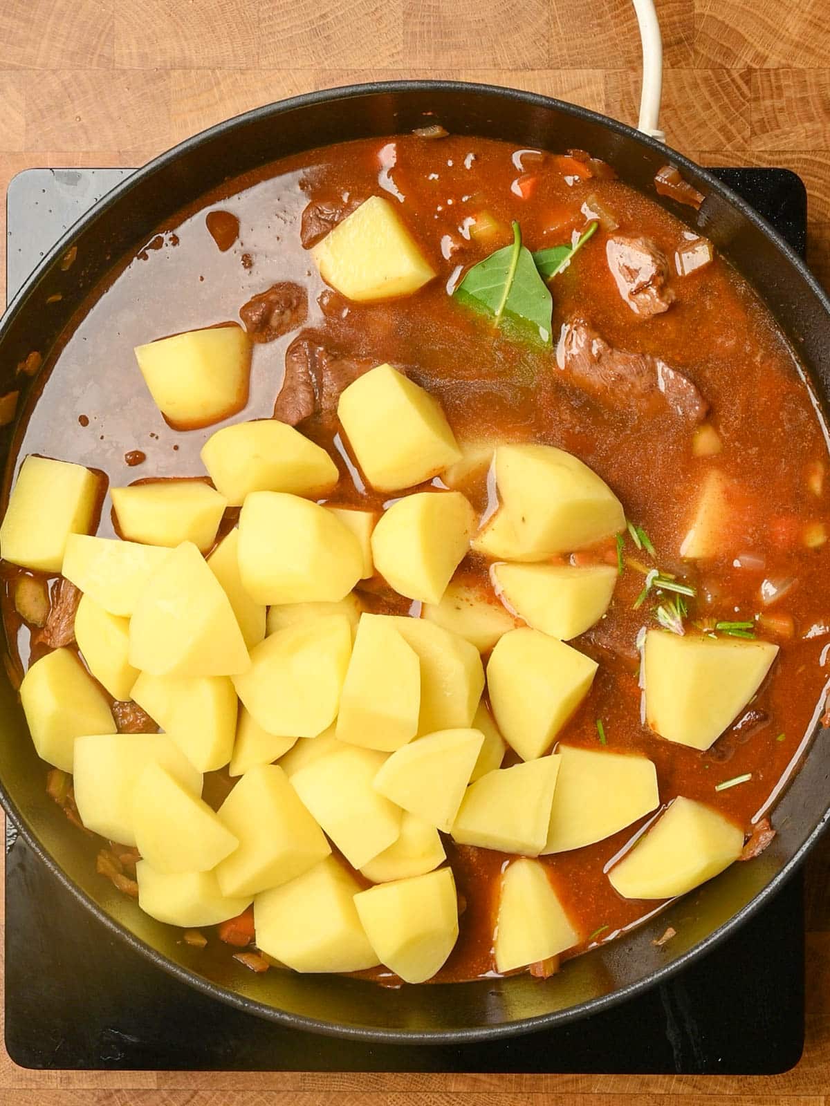 adding potatoes and stock to the cooking pan